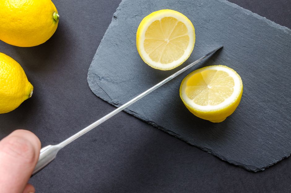 Top view of fresh lemons on a slate board with a knife, ready for slicing.